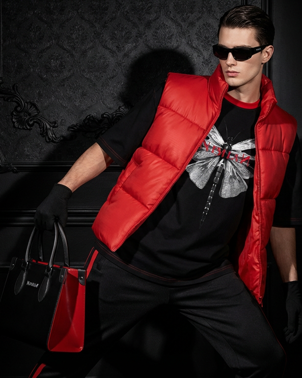 Person wearing a red puffer vest over a black outfit with a graphic design, standing against a dark background.